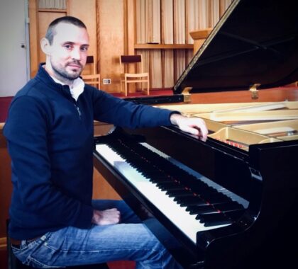 Image of Richard Maddux, seated at a piano on the right, with a backdrop of the church sanctuary